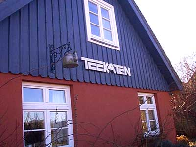 Der Darsser Teekaten in Wieck auf dem Darss. Sprossenfenster und Reetdach umgeben von Naturgarten.